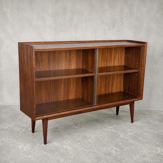 An elegant mid-century display cabinet combining walnut and teak tones with sliding glass doors. Set on tapered legs, its...