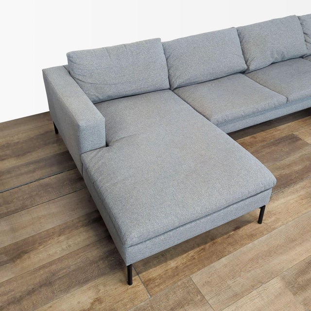 Features a modern design with wide arms, plush loose cushions, and distinctive angular powder-coated steel legs. Brand Blu...
