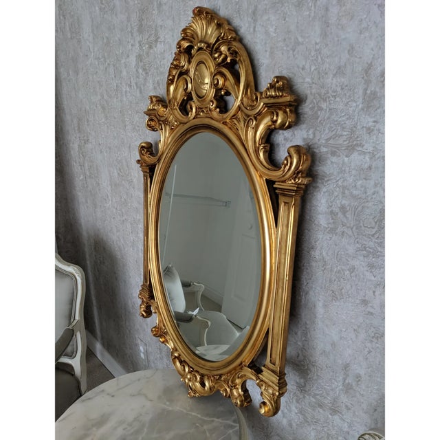 Italian rococo hand carved giltwood mirror featuring ornate filigree and gilding, scrolls, leaves, crests, and columns. No...
