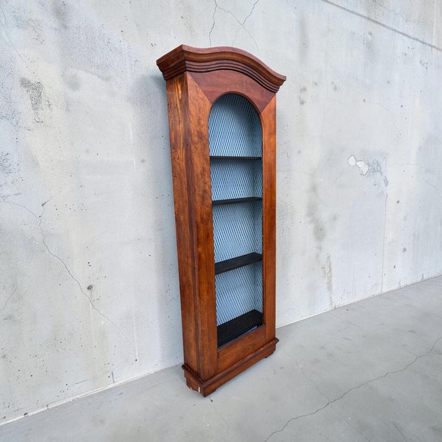 Striking antique wall-hanging display cabinet featuring an exceptionally tall, narrow profile, warm wood finish and an...