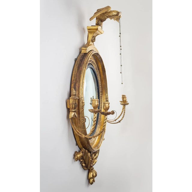 Large monumental classical gilded convex girandole mirror with strikingly well-carved dynamic eagle holding three chains,...