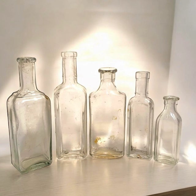 This early 20th century grouping includes five clear glass apothecary bottles with cork tops, each showing some cloudiness...