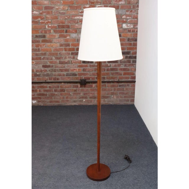 Simple, elegant floor lamp sculpted from solid teak with slender, cylindrical, tapered stem supported by dense round base...