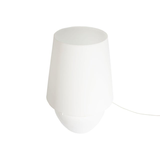 A white glass "Naxos" table lamp produced by Vistosi. Made in Italy, the lamp has a white glass shade and a white glass...