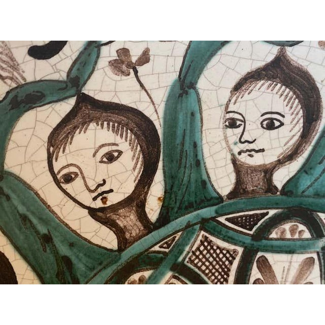 This hand-painted ceramic plate showcases a richly detailed design featuring a radial arrangement of stylized female...