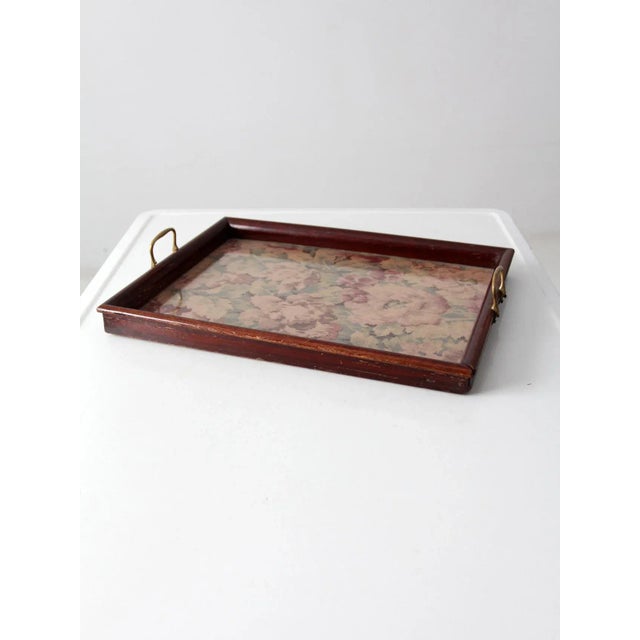 A vintage floral tray featuring a wooden frame and a glass-covered floral textile base. Brass handles add a warm metallic...
