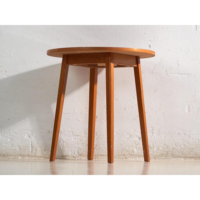 This vintage round side table in teak wood is a three-legged table with a circular top and tapered legs splayed outward....