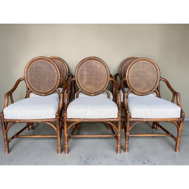 A set of six vintage rattan dining armchairs featuring classic oval cane backs and solid rattan frames with traditional...