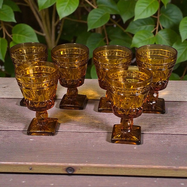 The product is a set of six vintage Indiana amber glass wine goblet glasses. These ornate goblets are perfect for all...