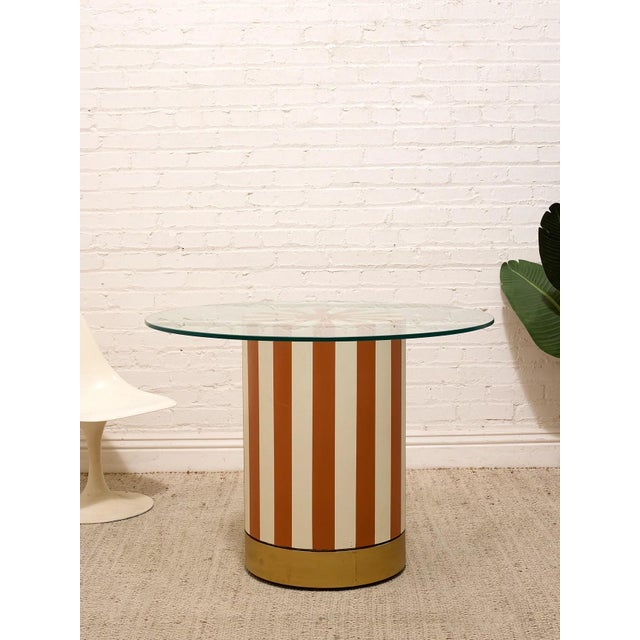 A playful statement dining table with a bold cylindrical pedestal wrapped in alternating burnt orange and cream stripes....