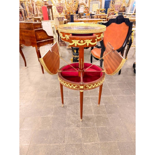 A striking French Louis XVI-style two-tier serving table featuring rich mahogany tones and beautifully detailed gilt...
