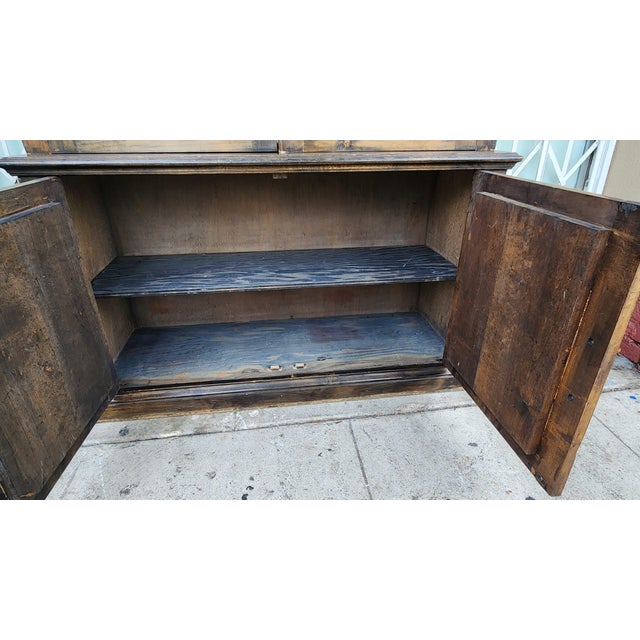 Ornate wooden display cabinet with a dark brown stained finish. This two-piece hutch has a top section with two glass-...