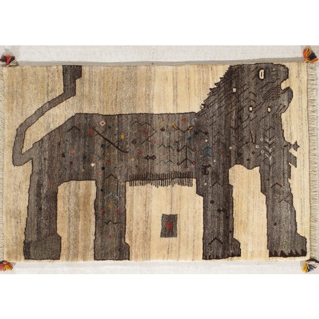 Vintage hand-knotted Persian Gabbeh wool rug featuring a stylized lion motif on an ivory field. The figure is outlined...