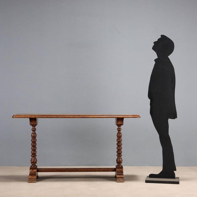 Console table in walnut-stained poplar. The top is supported by a pair of turned and carved legs, resting on molded feet...