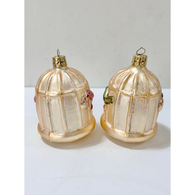Pair of vintage German glass Christmas ornaments shaped like birdcages, each featuring a small colorful bird perched...