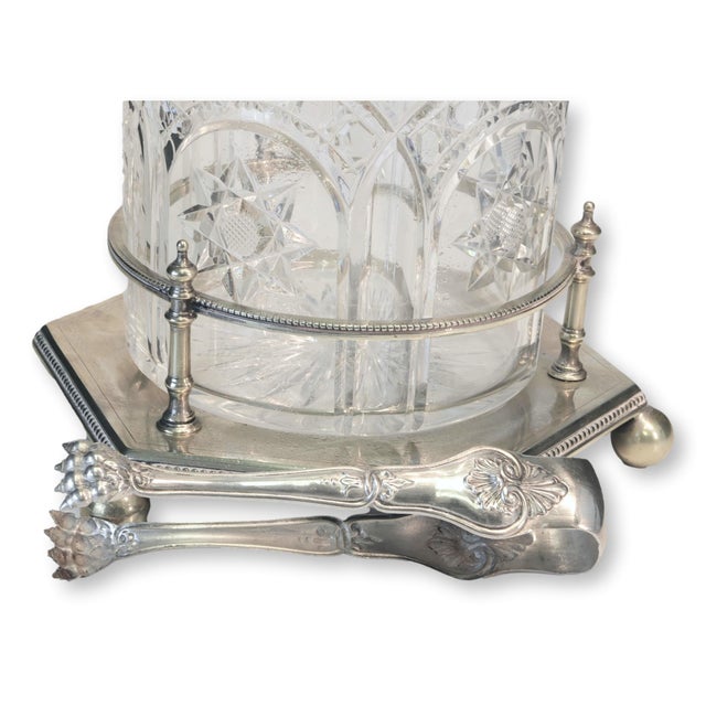 1920s English silver-plated and cut crystal ice bucket with tongs, resting on a raised footed base with beaded edging and...