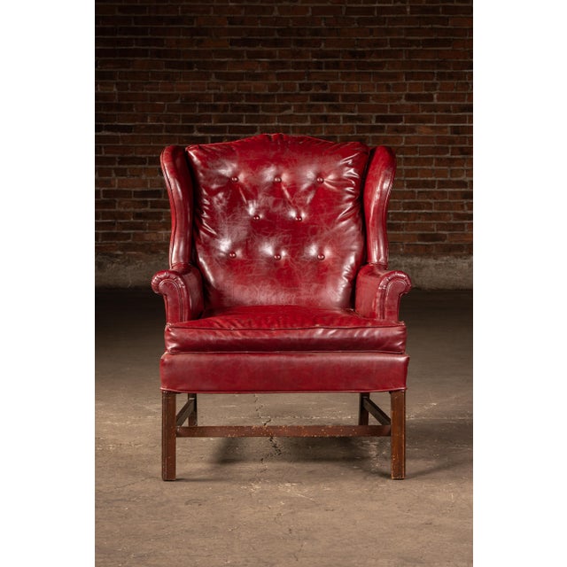 Classic wingback lounge chair upholstered in richly patinated red leather with a deeply button-tufted back, rolled arms,...