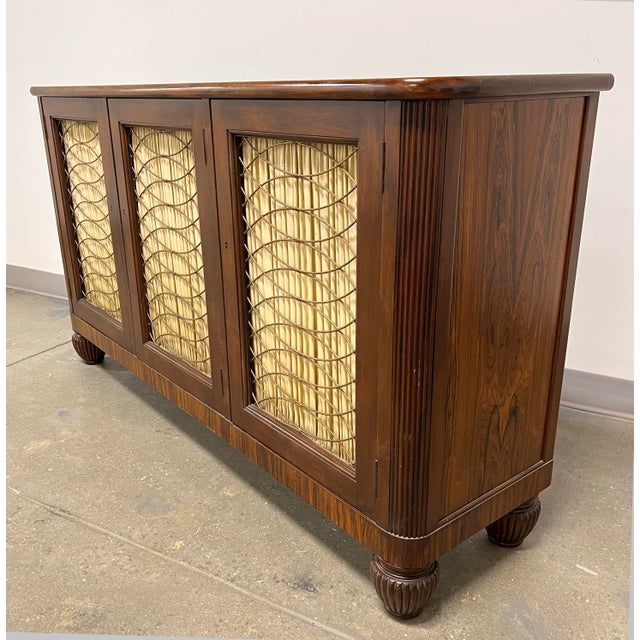 An English Regency style sideboard in rosewood with brass breakfront grillwork, circa 1950s. Inside features adjustable...