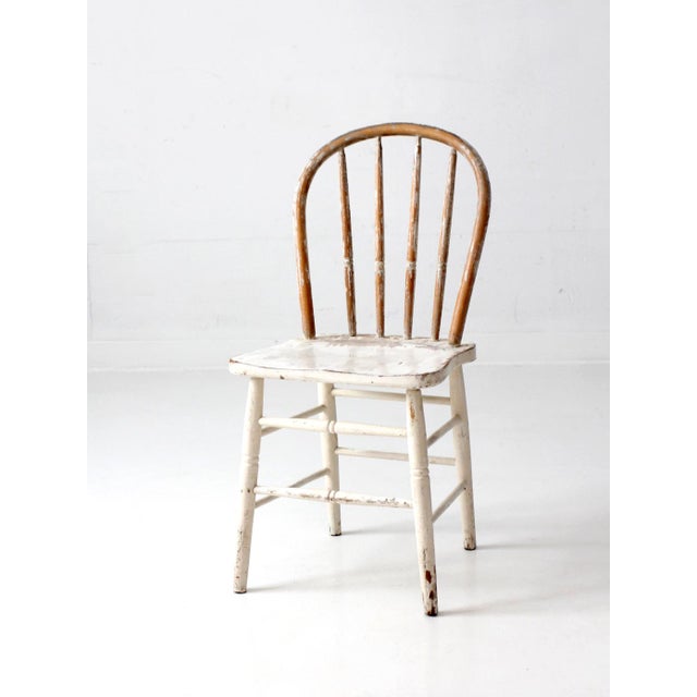 This vintage Windsor bow back chair features a beautifully worn white painted surface with exposed natural wood peeking...