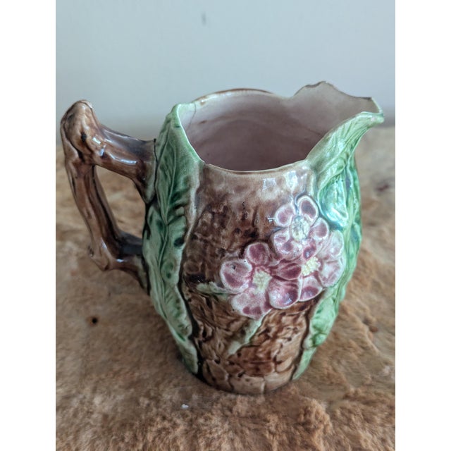 A delightful example of late 19th-century French majolica craft, this naturalistic pitcher features a trompe l'oeil tree...