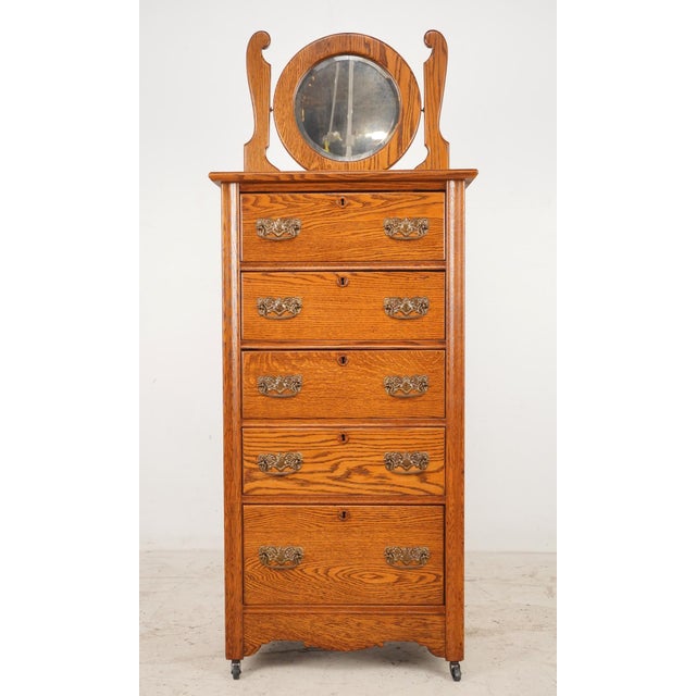 Vintage quarter sawn oak tall dresser with five dovetailed drawers and a beveled glass mirror. The curved mirror supports...