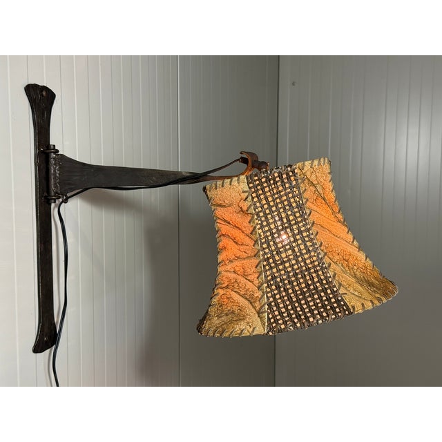 Lovely brutalist rustic wall lamp. Wrought iron wall fastening and swivelarm, original lampshade in leather, fabric and...