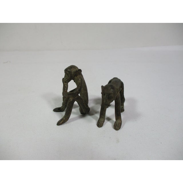 A vintage pair of hand-crafted bronze African monkey figurines. One monkey is sitting enjoying a banana and the other is...