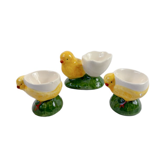 A charming set of three Bordallo Pinheiro ceramic egg cups modeled as yellow chicks perched on green grassy bases. Each...