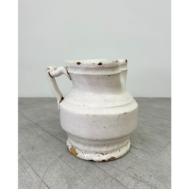 Antique hand-thrown jug in a soft creamy white glaze that is elegantly refined in its simplicity, highlighting the skill...