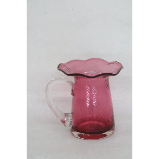 This gorgeous pitcher / vase is made of glass. This piece has a lovely cranberry / pink color to the glass with a clear...