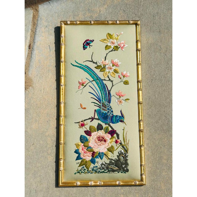 A beautifully framed embroidered textile artwork featuring a vibrant blue exotic bird perched among delicate blossoms and...