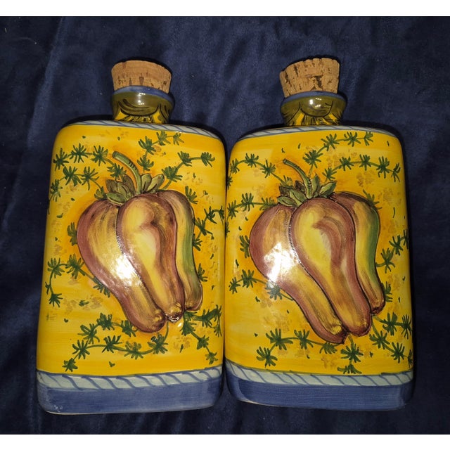 This image shows a pair of hand-painted ceramic cruets, typically used as a matching set for serving olive oil and...