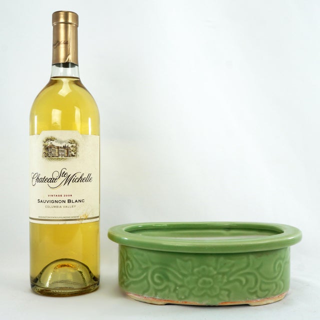 An oval Japanese bulb pot with a white interior and celadon exterior. The sides of the pot have incised decorations of a...