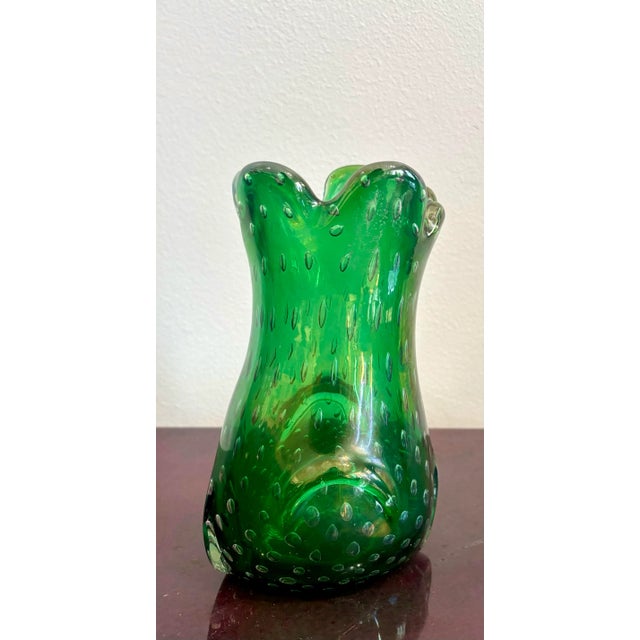 This vivid green art glass vase is a playful celebration of color and form. Its scalloped rim undulates like petals in...