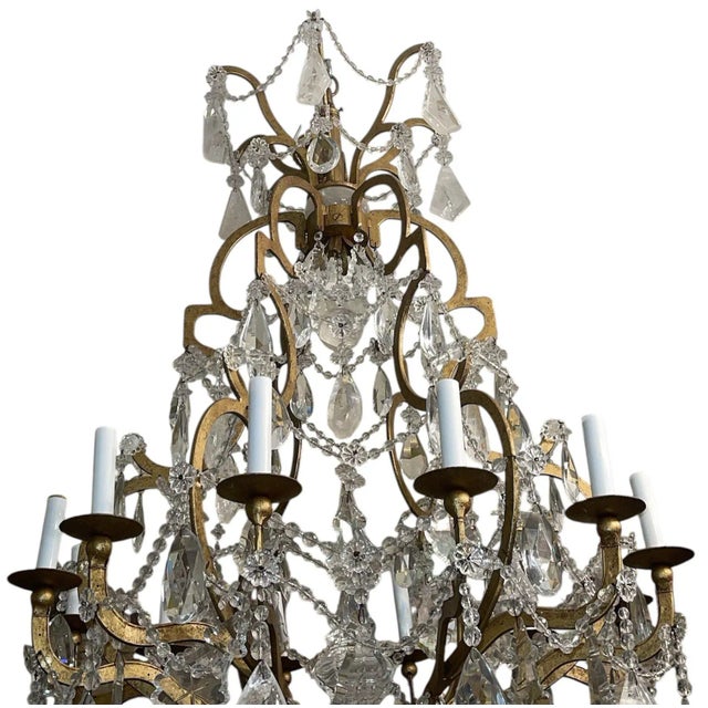 Elegant twelve-light chandelier composed of a hand-wrought gilt iron frame draped with rock-crystal drops, crystal prisms,...