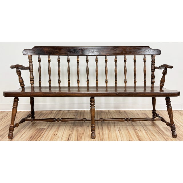 Wonderful vintage pine wood Windsor style bench featuring low back, turned wood arms, legs and stretchers, and ample seat....