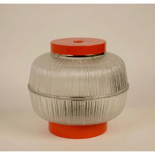 Table lamp with base and top in orange lacquered metal and corpus in heavy press glass. Manufactured in 1970s in...