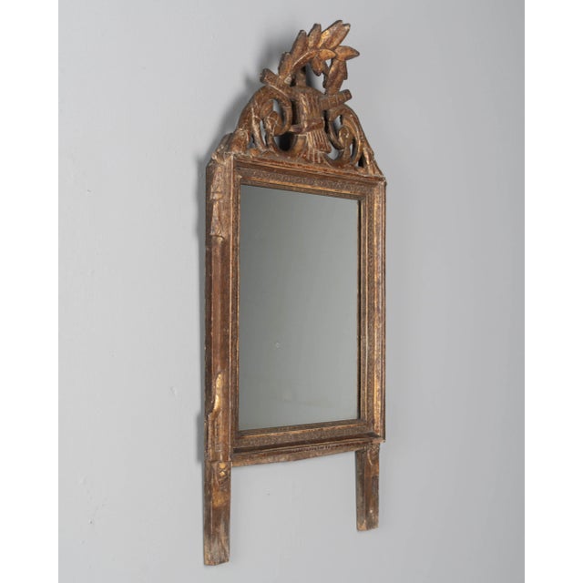 An early 19th century Louis XVI style French Provençal giltwood mirror. Hand carved crest with a swirl of garlands and...