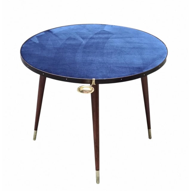 A refined and rare circular gaming table, made of wood with a top covered in a vibrant electric blue cloth. Along the edge...
