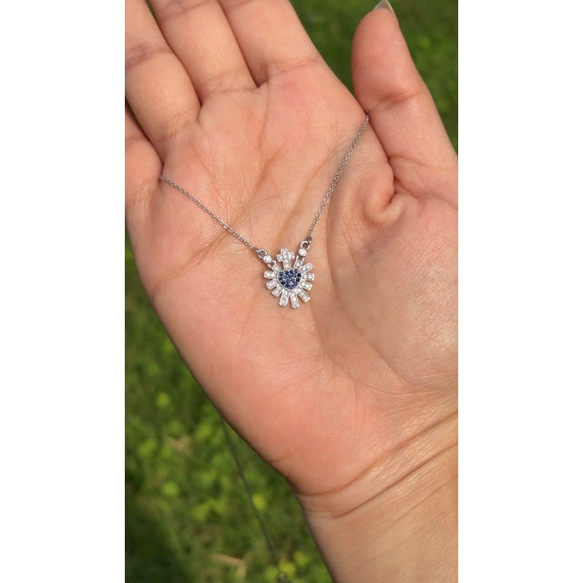 This Sacred Heart pendant necklace featuring a 0.15 carat round cut blue sapphire, crafted in 14K white gold. symbolic...