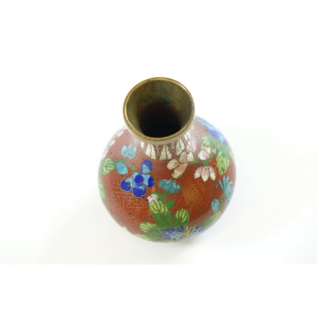 This early 20th-century Chinese cloisonné vase features a striking red base with a small opening and a larger body....