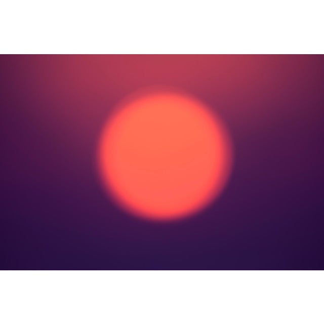 This photograph captures a softly blurred sun, radiating a warm, glowing orb against a gradient backdrop of deep purples...