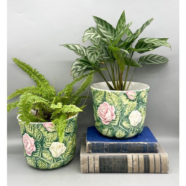 Pair of Italian ceramic cachepots with raised pink and cream roses set against dense green foliage in a majolica-style...