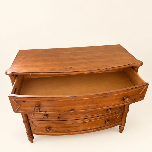 An Ethan Allen bowfront chest in warm pine, its four drawers framed by faux-bamboo turned columns and bamboo-carved...