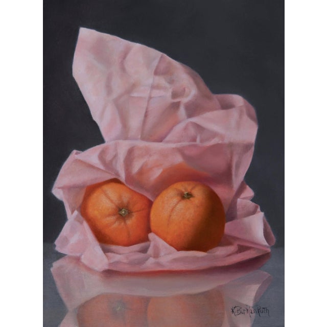 In "Papered in Pink," two vibrant oranges rest atop crumpled pink tissue, their glossy surfaces reflecting subtle light....