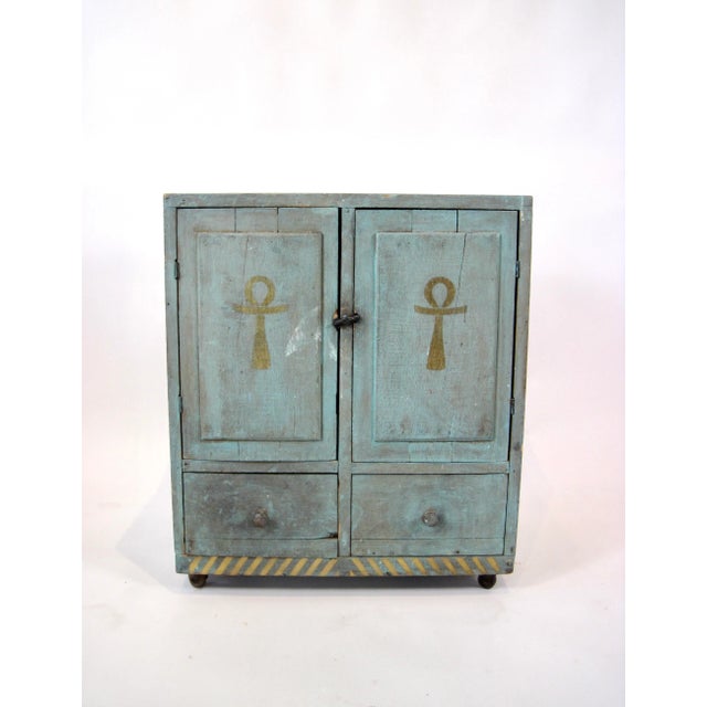 Folk Art, Outsider Art Reclaimed wood cabinet in teal/light verdigris with gold Egyptian symbols on castors. Two cabinet...