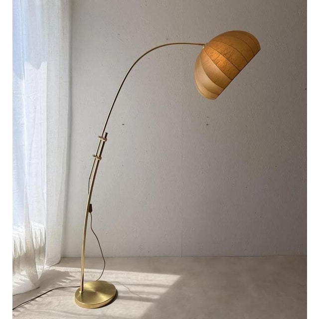 1970s arc lamp by Hustadt Leuchten, crafted in brass with a large semi-transparent cocoon shade. The tall, curved arm...