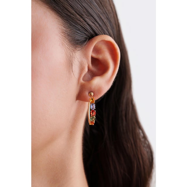 These half hoop earrings showcase 4.07 carats of natural oval cut rainbow sapphires, set in 14K yellow gold. Each...