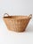 An antique wicker laundry basket with a broad oval shape, softly tapered sides, and two gracefully wrapped handles. The...