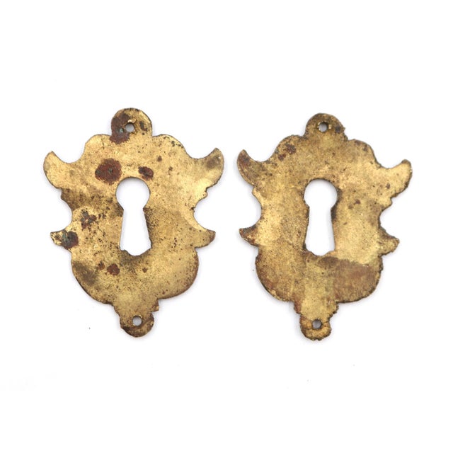 Traditional style brass keyhole covers with a symmetrical flourish shape. The original mounting screws are not available....